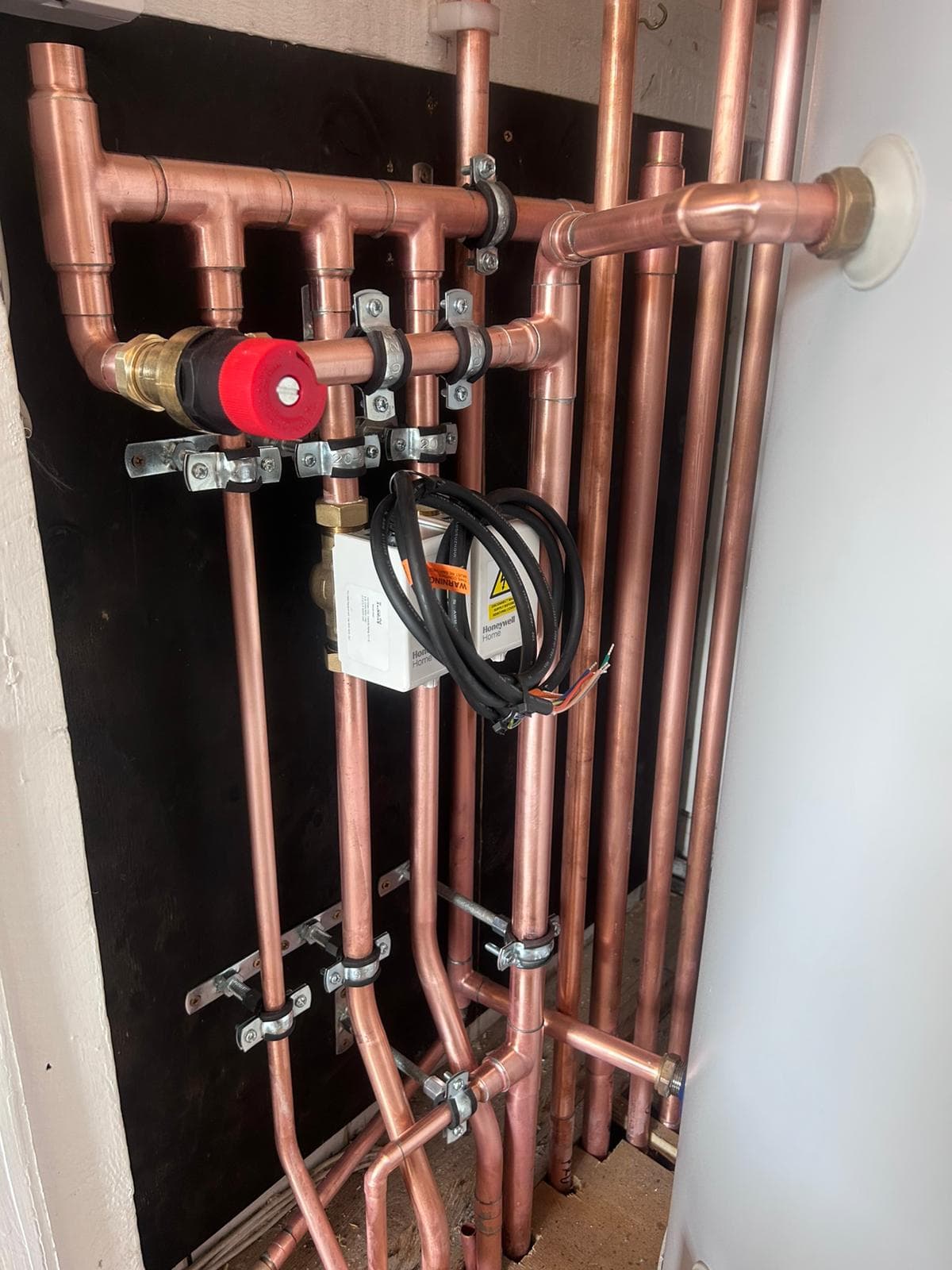 Close-up of bracket-mounted copper pipework with motorised zone valve, clipped at correct intervals